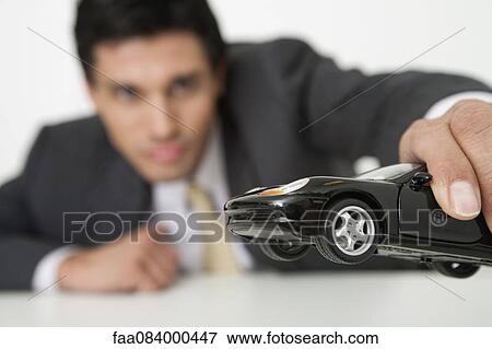 Stock Photo - Mid-adult businessman playing with toy car. Fotosearch