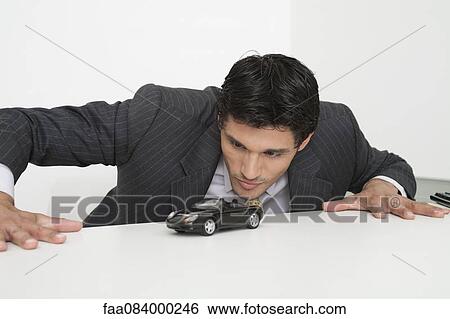 Mid-adult businessman staring at toy car View Large Photo Image Stock Photograph - Mid-adult businessman staring at toy car. Fotosearch