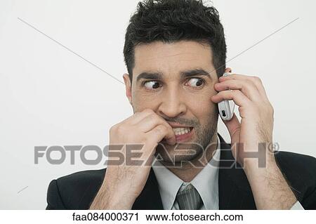 Stock Image - Mid-adult businessman talking on cell phone with anxious expression. Fotosearch