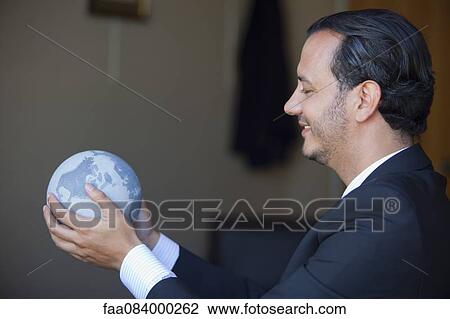 Stock Image - Mid-adult executive holding globe, side view. Fotosearch