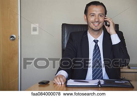 Stock Photo - Mid-adult executive talking on cell phone in office. Fotosearch