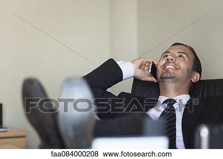Mid-adult executive talking on cell phone with legs on desk View Large Photo Image Stock Photo - Mid-adult executive talking on cell phone with legs on desk. Fotosearch