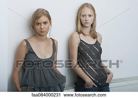 Stock Image - Teenage girl and young woman leaning against wall, portrait. Fotosearch