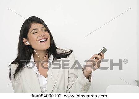 Stock Image - Young businesswoman listing to music on mp3 player. Fotosearch