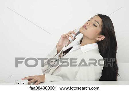 Stock Image - Young businesswoman talking on landline phone. Fotosearch
