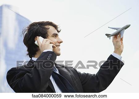 Young executive holding toy airplane while talking on cell phone View Large Photo Image Stock Photo - Young executive holding toy airplane while talking on cell phone. Fotosearch