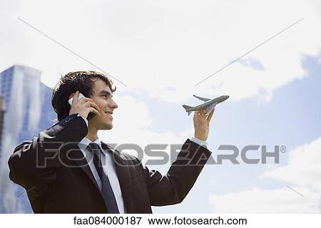 Young executive holding toy airplane while talking on cell phone View Large Photo Image Stock Photo - Young executive holding toy airplane while talking on cell phone. Fotosearch