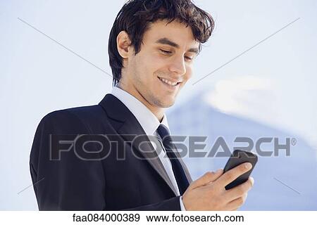 Stock Photo - Young executive text messaging outdoors. Fotosearch