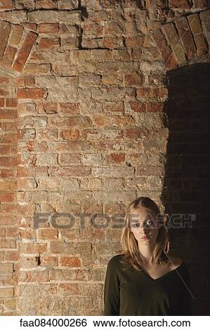 Stock Photograph - Young woman in front of brick wall, portrait. Fotosearch