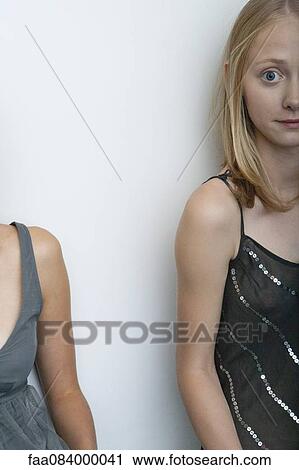 Stock Image - Young woman leaning against wall, cropped portrait. Fotosearch