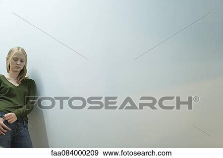 Stock Photo - Young woman leaning against wall, looking down. Fotosearch