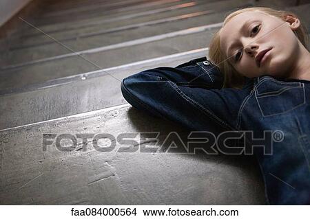 Picture - Young woman lying on stairs with hands behind head, portrait. Fotosearch