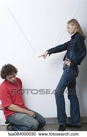 Stock Image - Young woman pointing at man kneeling before her. Fotosearch