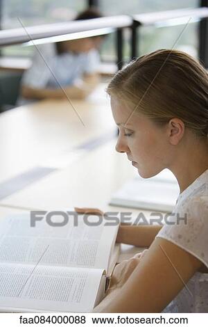 Stock Photo - Young woman reading book in library. Fotosearch