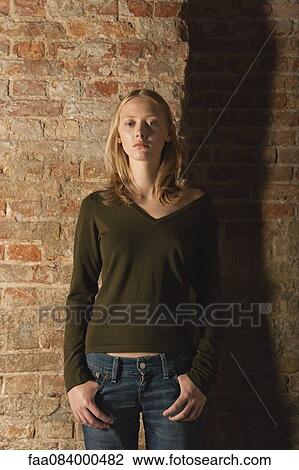 Stock Image - Young woman standing with hands in pockets, portrait. Fotosearch