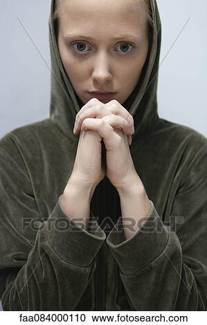 Stock Image - Young woman with hands clasped in prayer, portrait. Fotosearch