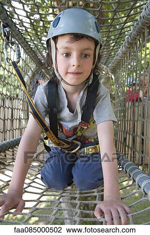 Stock Image - Boy climbing through net in playground tunnel. Fotosearch