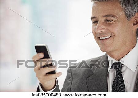 Stock Photo - Business executive looking at cell phone, smiling. Fotosearch