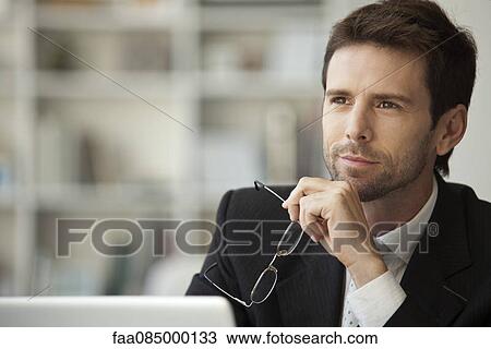 Businessman looking away in thought, glasses in hand View Large Photo Image Stock Image - Businessman looking away in thought, glasses in hand. Fotosearch