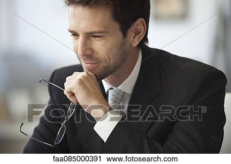 Stock Image - Businessman looking away in thought, glasses in hand. Fotosearch
