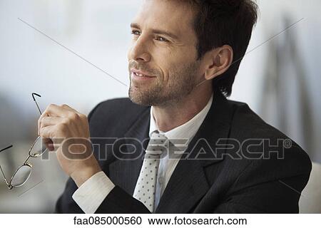 Businessman looking away in thought, glasses in hand View Large Photo Image Stock Image - Businessman looking away in thought, glasses in hand. Fotosearch