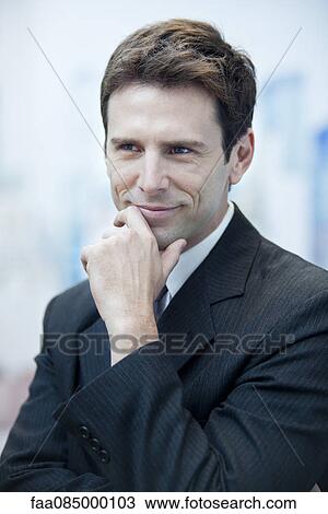 Stock Image - Businessman smiling and looking away in thought, portrait. Fotosearch
