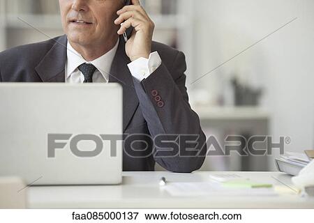 Businessman talking on cell phone and using laptop computer, cropped View Large Photo Image Stock Photo - Businessman talking on cell phone and using laptop computer, cropped. Fotosearch