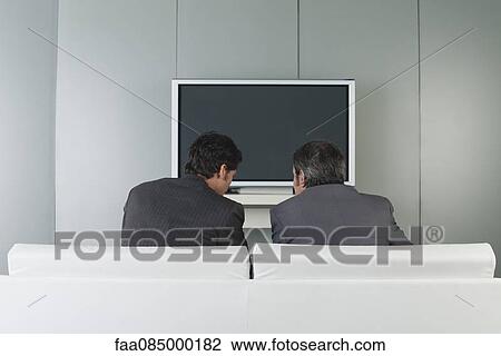 Businessmen sitting on couch in front of television View Large Photo Image Stock Image - Businessmen sitting on couch in front of television. Fotosearch