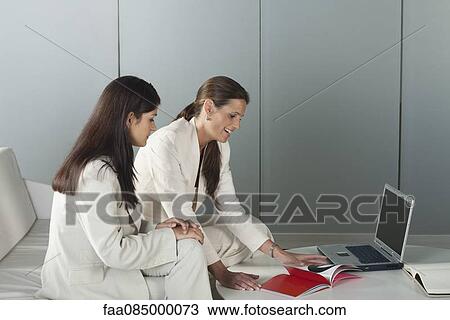 Stock Image - Businesswomen reading magazine together. Fotosearch