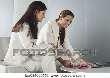 Stock Image - Businesswomen reading magazine together. Fotosearch