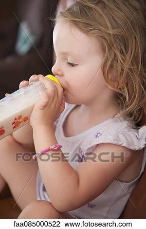 Stock Image - Little girl drinking milk from bottle, side view. Fotosearch
