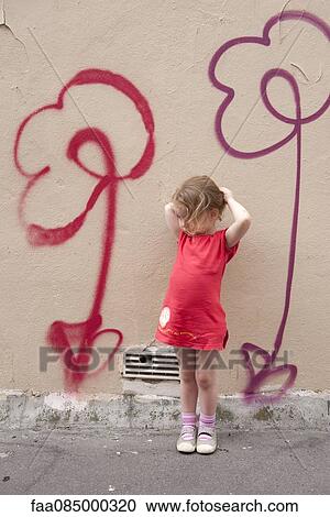 Stock Image - Little girl leaning against wall with flower graffiti, portrait. Fotosearch
