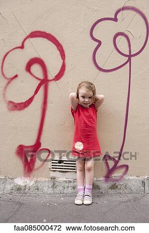Stock Image - Little girl leaning against wall with flower graffiti, portrait. Fotosearch