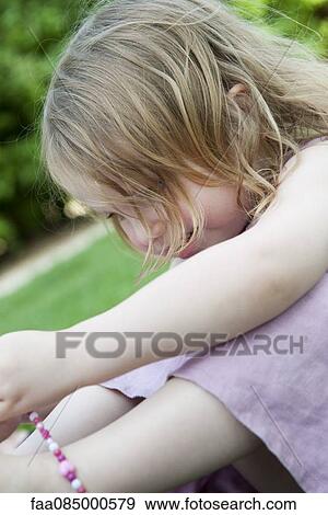 Stock Photo - Little girl sitting outdoors, playing with beaded necklace. Fotosearch