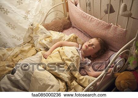 Stock Photograph - Little girl sleeping in bed, high angle view. Fotosearch