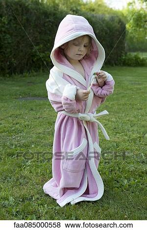 Stock Photo - Little girl standing outdoors in oversized bathrobe, holding dandelion stem. Fotosearch
