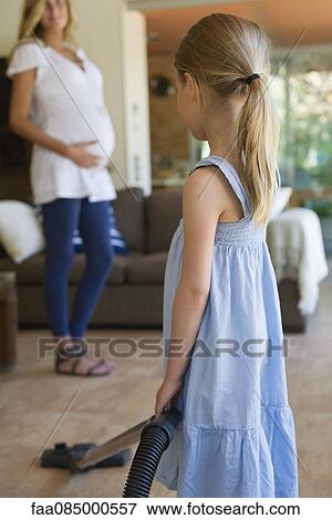 Stock Photo - Little girl vacuuming, pregnant mother in background. Fotosearch