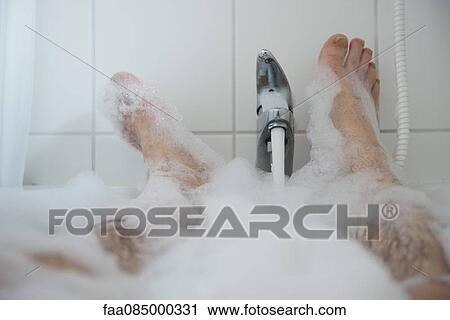 Stock Image - Man soaking in bubble bath, low section. Fotosearch