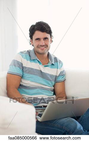 Stock Photograph - Man using laptop computer at home, portrait. Fotosearch