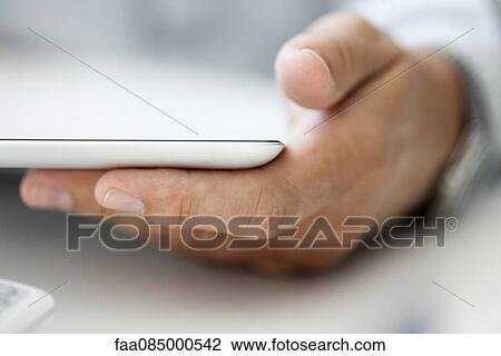 Stock Image - Man's hand holding digital tablet, close-up. Fotosearch