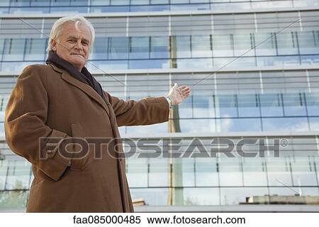 Mature businessman gesturing proudly toward building, portrait View Large Photo Image Stock Photography - Mature businessman gesturing proudly toward building, portrait. Fotosearch