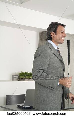 Stock Photograph - Mature businessman holding golf club. Fotosearch