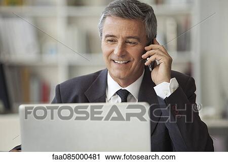 Mature businessman talking on cell phone and using laptop computer View Large Photo Image Stock Image - Mature businessman talking on cell phone and using laptop computer. Fotosearch