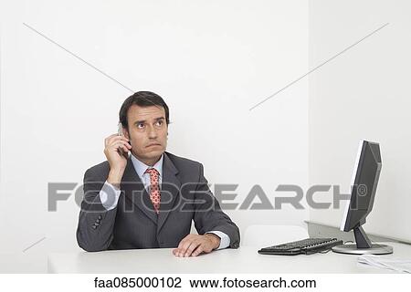 Stock Image - Mature businessman using cell phone at desk. Fotosearch