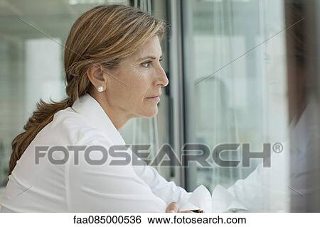 Stock Photograph - Mature woman looking out window, portrait. Fotosearch