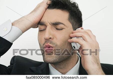 Stock Photograph - Mid-adult businessman talking on cell phone with frustrated look. Fotosearch