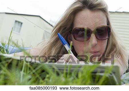 Woman lying on grass, writing View Large Photo Image Stock Image - Woman lying on grass, writing. Fotosearch