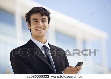 Stock Image - Young executive using cell phone outdoors. Fotosearch
