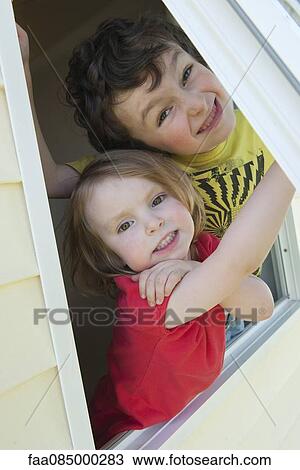 Stock Image - Young siblings looking out open window, portrait. Fotosearch