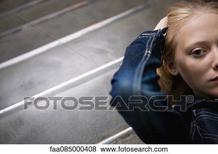 Stock Photo - Young woman lying on stairs with hands behind head, portrait. Fotosearch